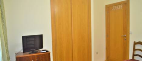 A room with a wooden wardrobe, a television on a wooden cabinet, and a red chair.
