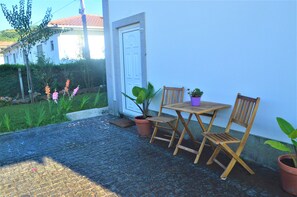 An outdoor patio with a wooden table and chairs, potted plants, and a door to a building. - Casa Límia (Ponte de Lima)