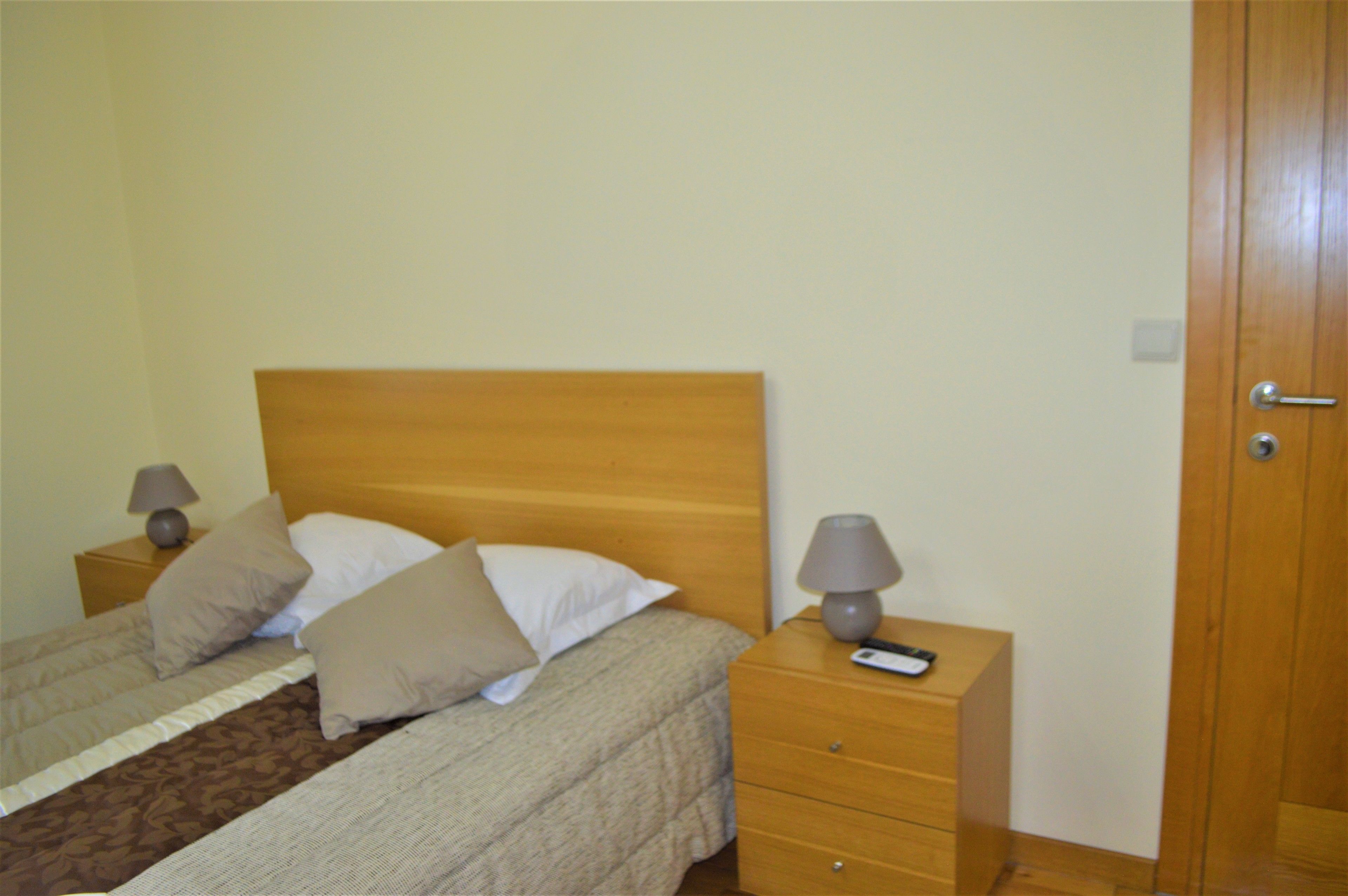 A double bed with a wooden headboard, two bedside tables with lamps, and a wooden door.