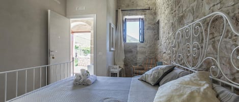 Une chambre avec un mur en pierre, un cadre de lit en métal et une vue sur l’extérieur par une fenêtre.