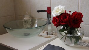 Et badeværelse med en vask i glas og en vase med røde og hvide roser på bordet.
