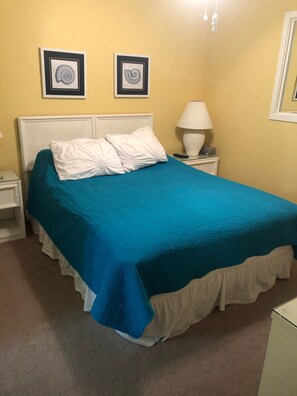 A bed with a blue and white bedspread, white pillows, and a white headboard. There are two framed pictures on the wall above the bed. - S. Myrtle Beach Resort 135 steps to sand  (Myrtle Beach)