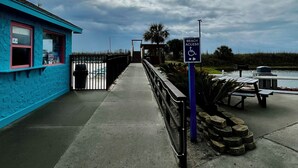 A pathway leading to a beach area with a blue building, a trash bin, and picnic tables. - S. Myrtle Beach Resort 135 steps to sand  (Myrtle Beach)