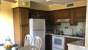 A kitchen with wooden cabinets, a white refrigerator, a microwave, an oven, and a dining table with chairs. - S. Myrtle Beach Resort 135 steps to sand  (Myrtle Beach)