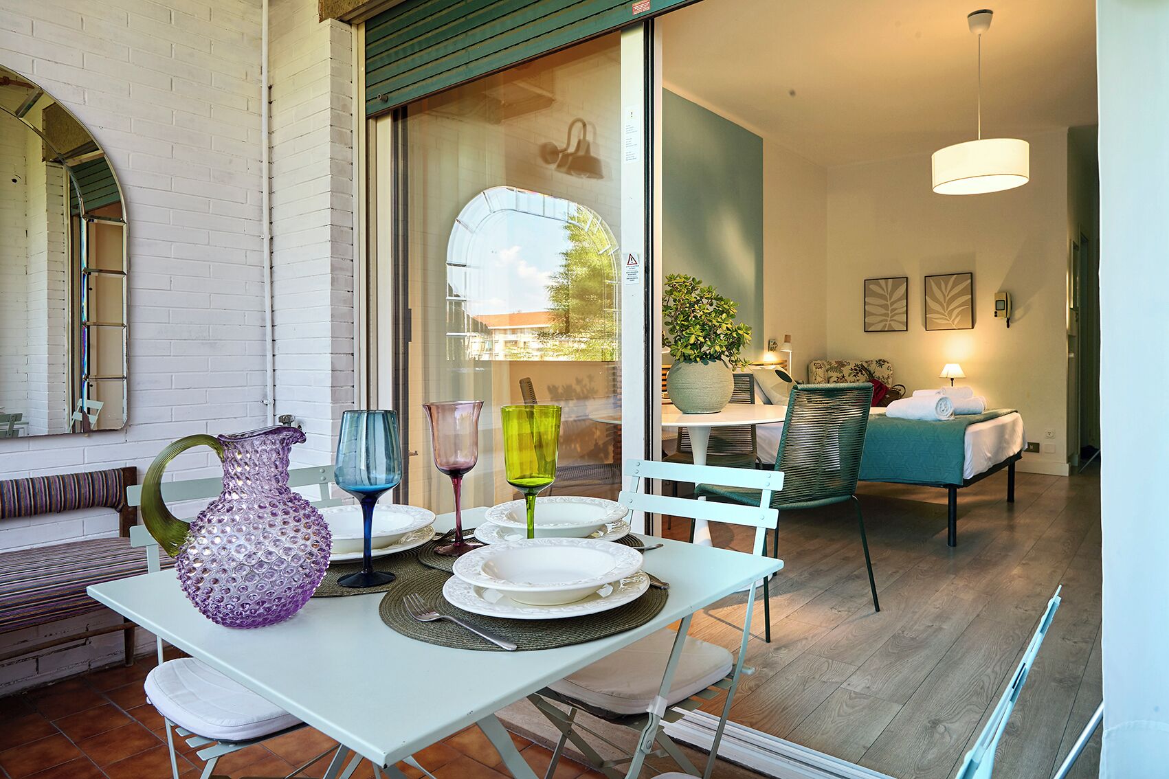 A dining area with a table set for two, a bench, and a view of the adjacent room.