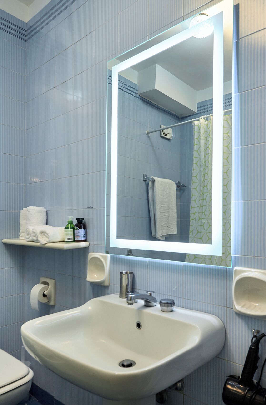 A bathroom with a white sink, a mirror, a towel rack, and a shelf with toiletries.