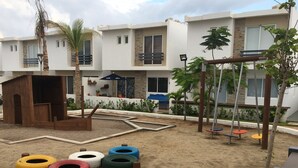 Ein Spielplatz mit Reifen-Schaukeln, einem hölzernen Spielhäuschen und einem Sandkasten.