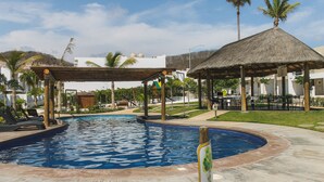 Ein Swimmingpool mit einem strohgedeckten Pavillon und Liegestühlen.
