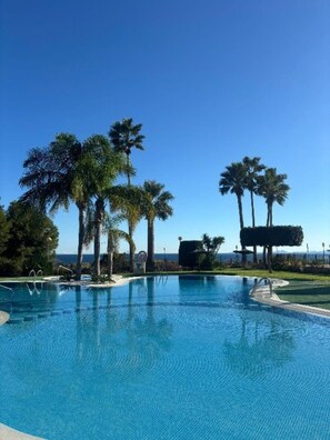 Piscina azul cristalina com palmeiras e vista para o oceano.