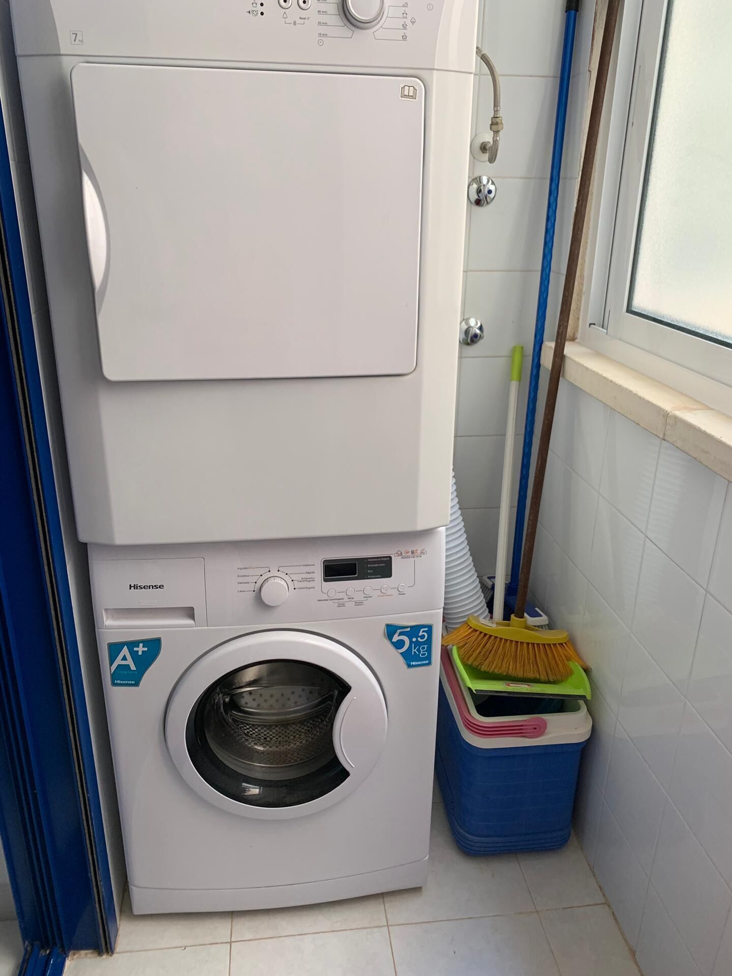 A stacked washer and dryer unit with a control panel, a small window, and a mop leaning against the wall.