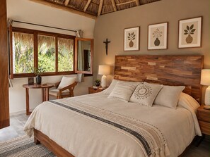 A bedroom with a bed, bedside tables, a chair, a window with a view of greenery, and framed artwork on the wall.