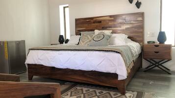 Un dormitorio con cabecera de madera, cama con ropa de cama blanca, mesita de noche con un reloj y aire acondicionado instalado en la pared.