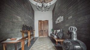 A hallway with wooden walls, a patterned rug, a chandelier, a wooden door, a sofa with decorative pillows, and a large vase. - A Villa San Juan Bed & Breakfast (Nuevo Nayarit)