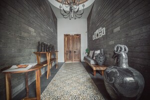 Un pasillo con paredes de madera, un tapete estampado, un candelabro, una puerta de madera, un sofá con cojines decorativos y un jarrón grande.