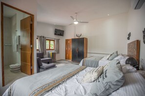 Une chambre avec deux lits, une armoire en bois, une télévision et un ventilateur de plafond.