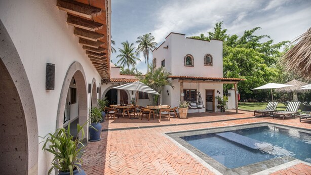 A courtyard with a swimming pool, outdoor seating, and a white building with arched doorways. - A Villa San Juan Bed & Breakfast (Nuevo Nayarit)