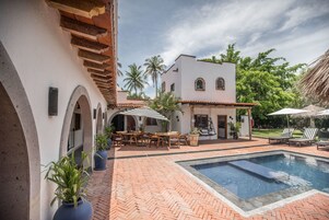 Un patio con piscina, mobiliario exterior y un edificio blanco con arcos.