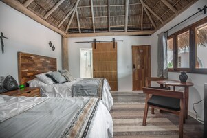 Un dormitorio con cabecera de madera, cama con ropa de cama estampada, escritorio con silla y un ventanal con vistas.