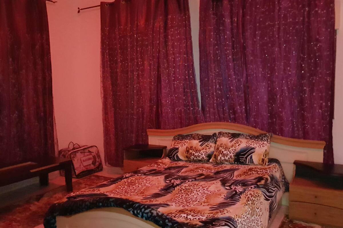 A bedroom with a bed, a nightstand, a lamp, and a window with curtains.