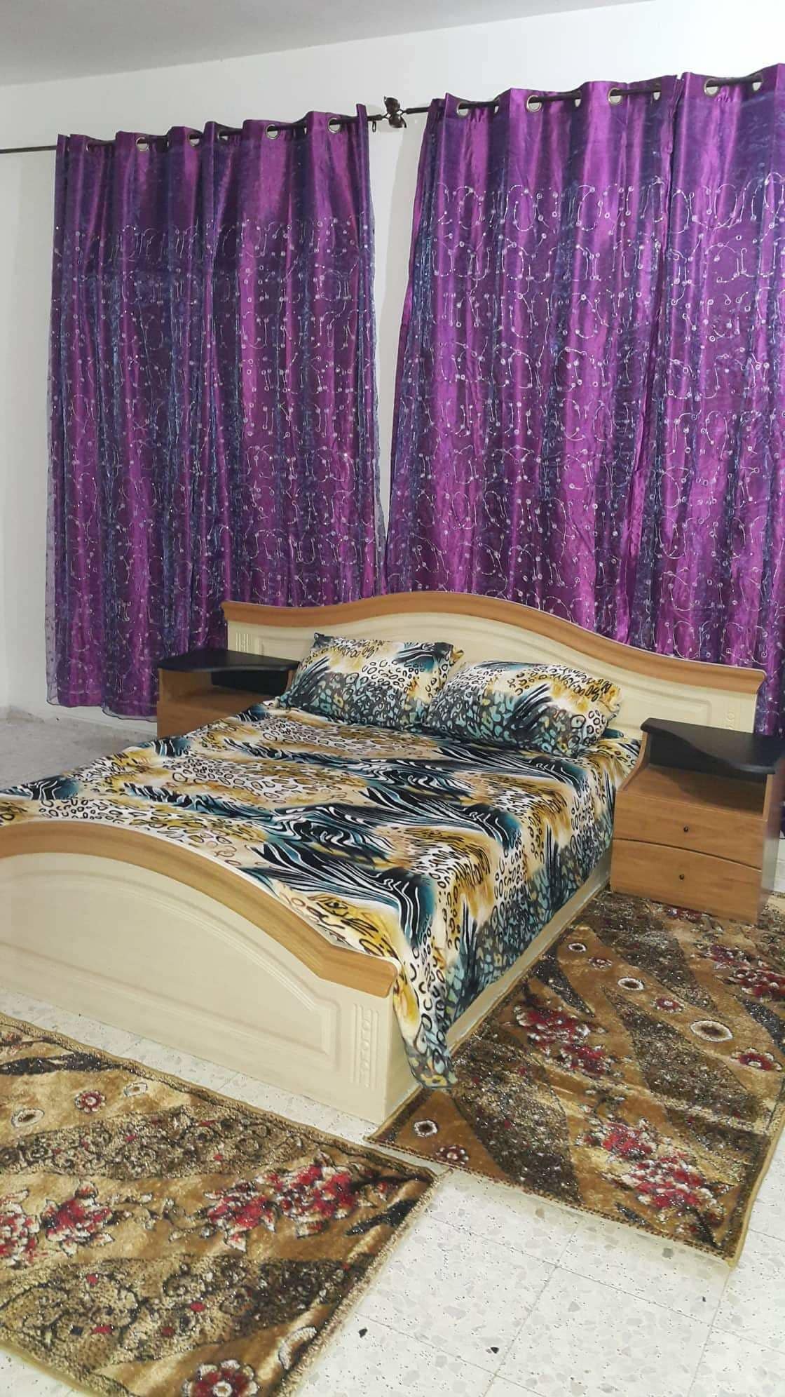 Ein Schlafzimmer mit einem Bett, zwei Nachttischen und violetten Vorhängen.