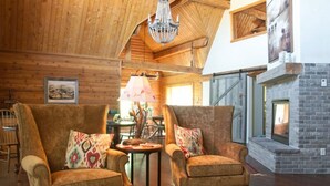 A cozy room with two armchairs, a chandelier, a fireplace, and wooden walls.