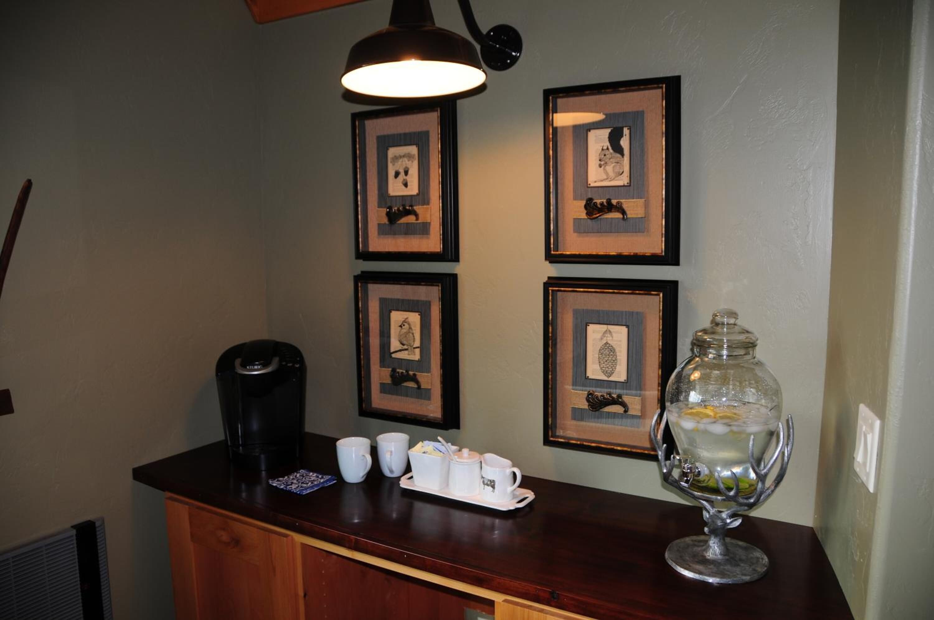 Un coin bar équipé d’une machine à café, d’un plateau avec des tasses et un sucrier, ainsi que d’un récipient en verre décoratif.