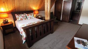 Un dormitorio con techo de madera, una cama con ropa de cama floral, dos lámparas de noche, una mesita de noche de madera y un aparador de madera.