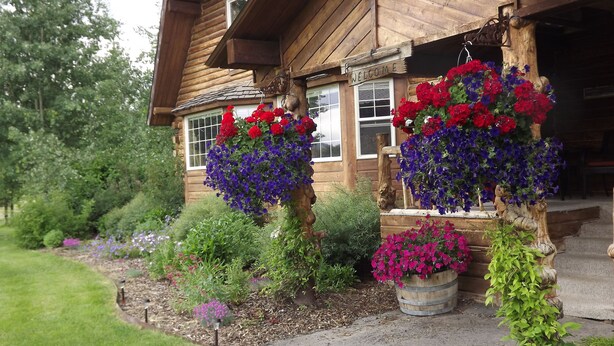 A wooden cabin with a welcoming sign, surrounded by lush gardens and various flower arrangements.