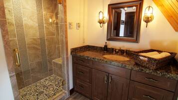 A bathroom with a shower, granite countertop, wooden cabinets, and a large mirror.