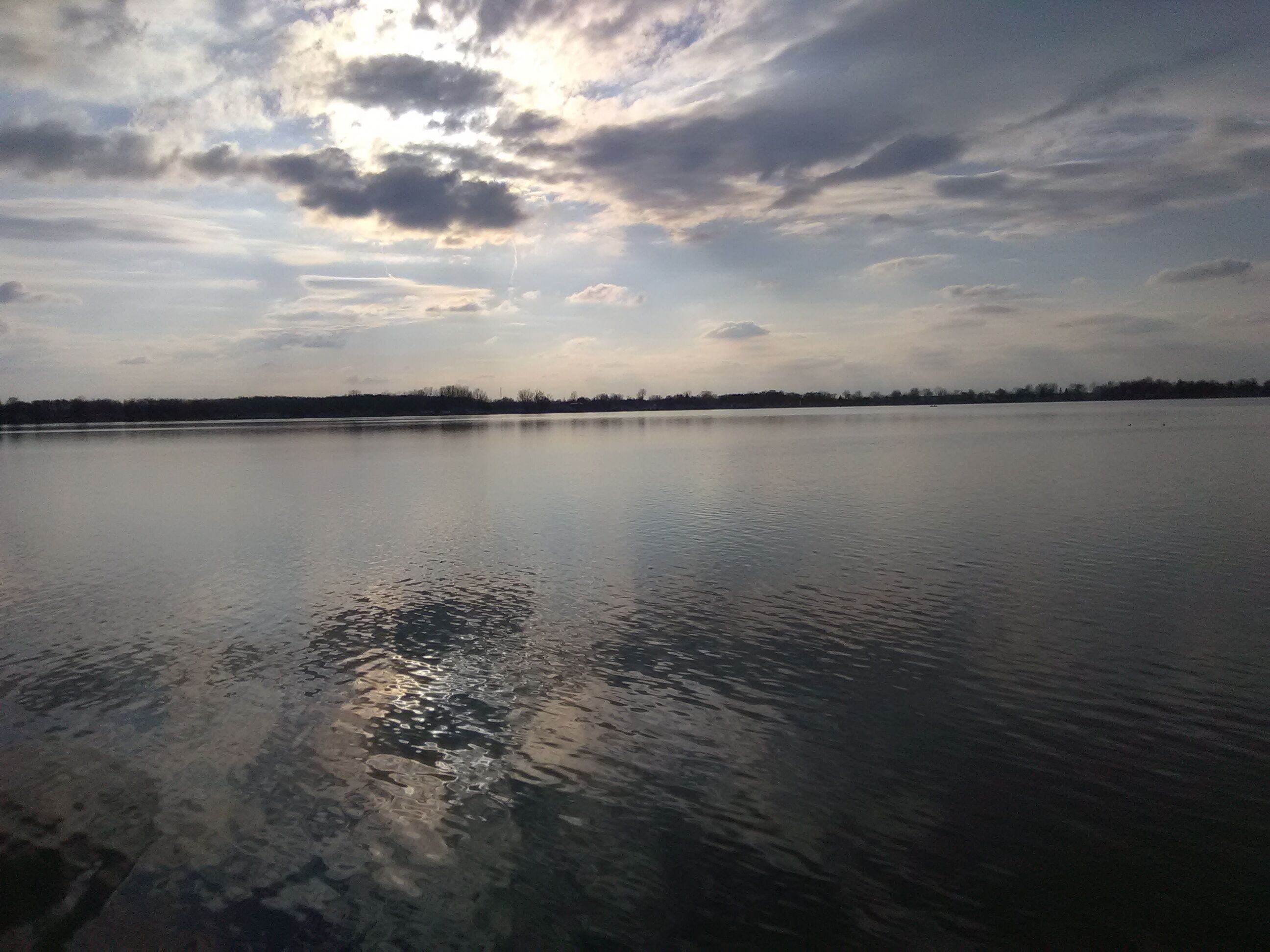 A calm lake with a distant tree line under a cloudy sky.