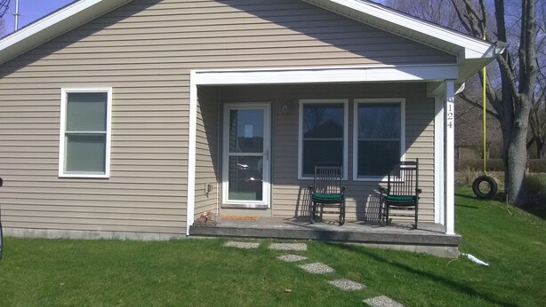 A single-story house with a front porch, two windows, and a door. - Orchard Lane at Round Lake. (Manitou Beach)