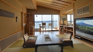 A modern living room with a large TV, wooden furniture, and a view of the sea.