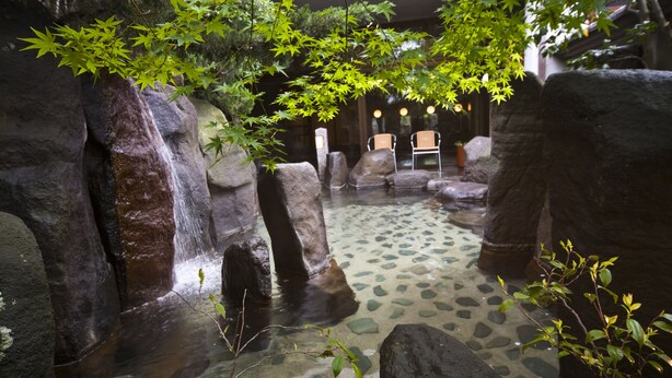 A serene indoor garden with a clear water feature, large rocks, and seating areas.