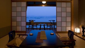 A traditional Japanese room with tatami flooring, a low table with cushions, and a view of a body of water.