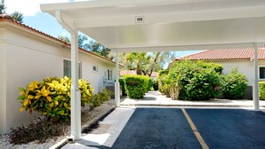 A covered parking area with numbered parking spaces, adjacent buildings, and well-maintained greenery. - Beachy villa on Siesta Key with heated pool, screened in lanai, and ground level (Sarasota)