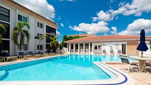 A swimming pool with lounge chairs and umbrellas, a building with a tiled roof, and palm trees. - Beachy villa on Siesta Key with heated pool, screened in lanai, and ground level (Sarasota)