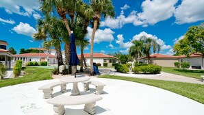 A courtyard with a white table and chairs, surrounded by palm trees and a clear blue sky. - Beachy villa on Siesta Key with heated pool, screened in lanai, and ground level (Sarasota)