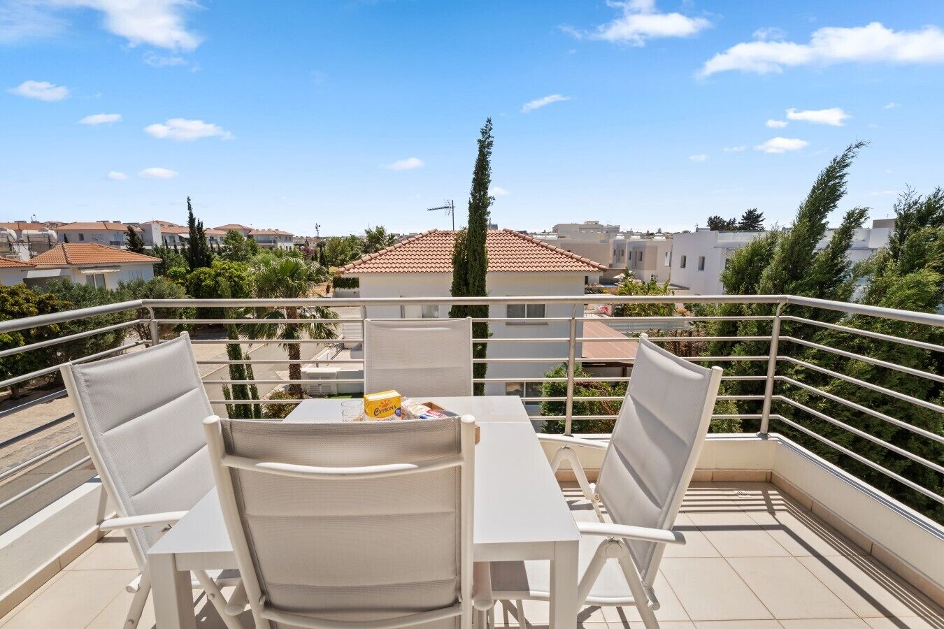 Ein Balkon mit zwei weißen Stühlen und einem Tisch, mit Blick auf eine Wohngegend mit Häusern und Bäumen.