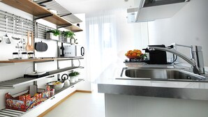 Et moderne køkken med indbyggede apparater, en stålvask og diverse køkkenredskaber samt kogegrej på åbne hylder.