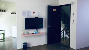 A room with a flat-screen TV on a pink shelf, a black door, and a staircase in the background. - Aegean Sea Homestay (Magong)