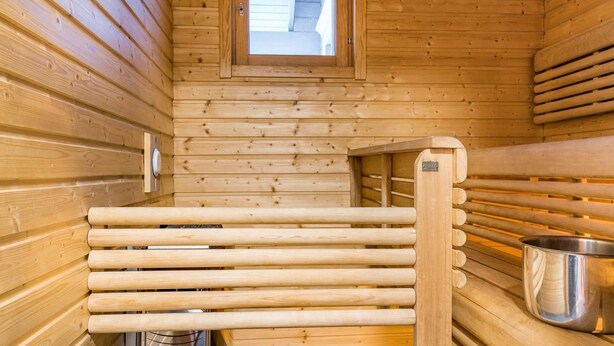 A sauna with wooden walls, a bench, a metal container, and a small window.