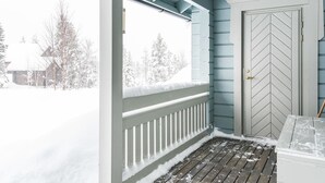 A covered porch with a view of a snowy landscape, a door with a chevron pattern, and a wooden deck.