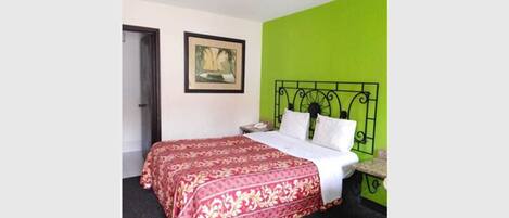 Un dormitorio con cama, pared verde, un cuadro enmarcado y una puerta.