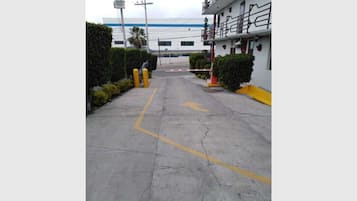 A hotel entrance with a concrete pathway leading to a building. There are yellow bollards and a yellow directional arrow on the ground.