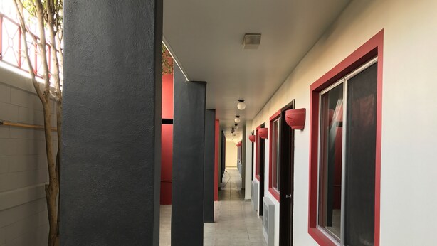 Un pasillo con ventanas de marco rojo, pilares negros y suelo de baldosas.
