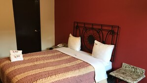 Una habitación de hotel con una cama, una mesita de noche, una silla y una pared roja.