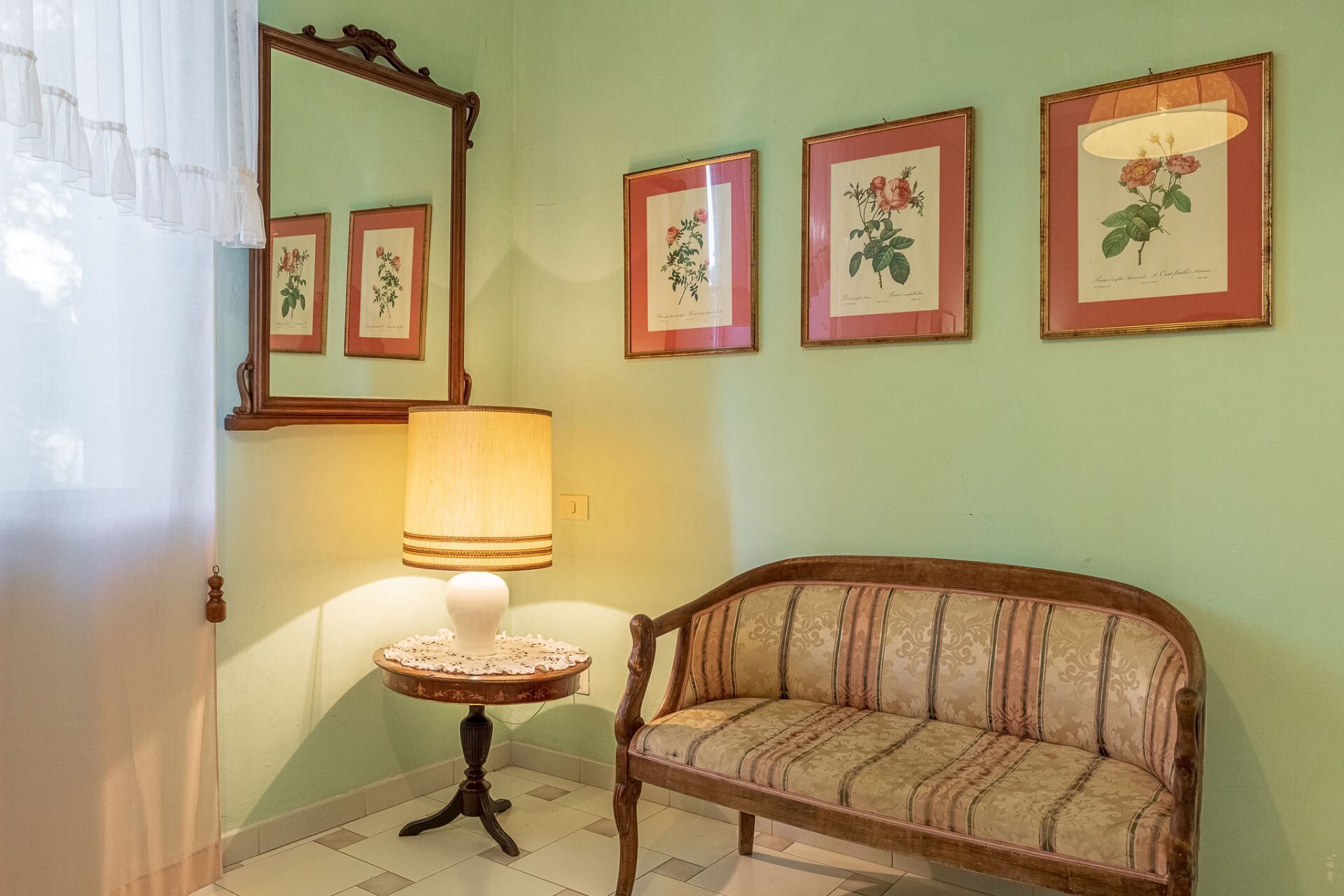 A room with a sofa, a table with a lamp, and framed botanical prints on the wall.