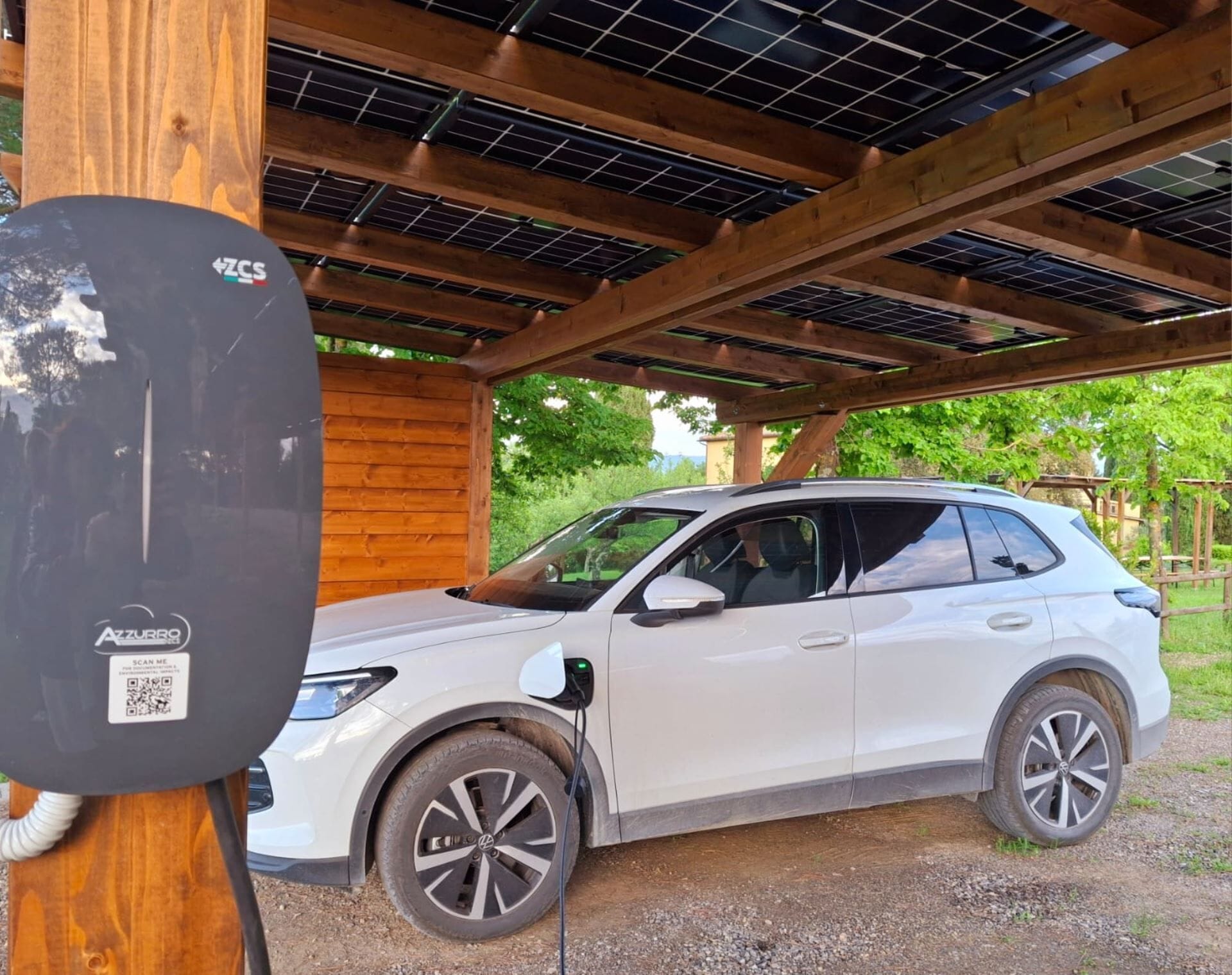 A white SUV parked under a wooden structure with solar panels on the roof.
