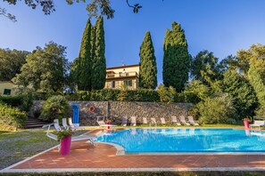 A swimming pool with lounge chairs, a stone wall, and tall trees.