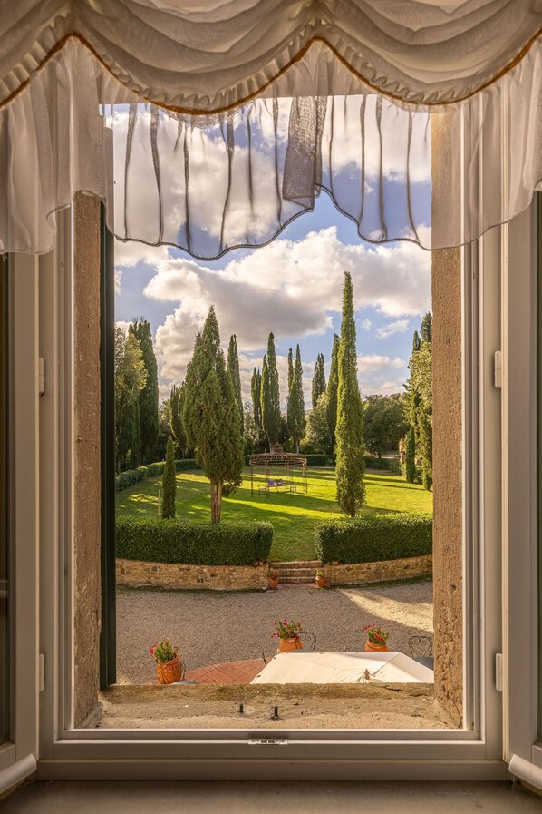 A window with a view of a well-manicured garden, including hedges and trees.
